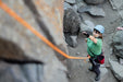 Person rock climbing with a helmet and safety rope on a rocky outdoor setting.