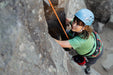Person rock climbing with a helmet and harness on a rocky wall.