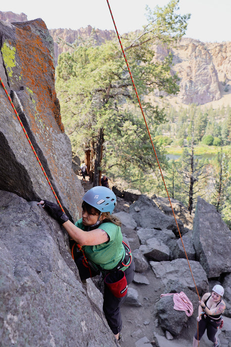 Person climbing a rocky cliff with another person observing below.