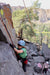 Person climbing a rocky cliff with another person observing below.
