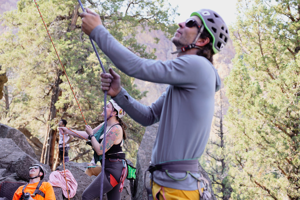 Person rock climbing with others in a forest setting.