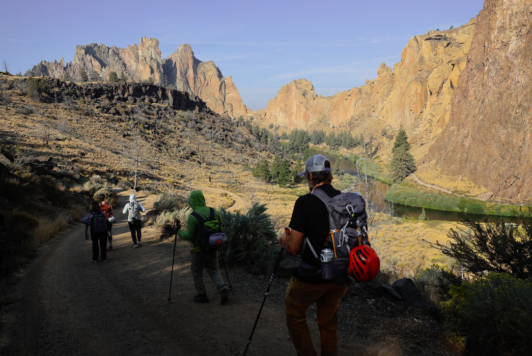 Hikers on a trail with rocky cliffs and mountains in the background
