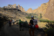 Hikers on a trail with rocky cliffs and mountains in the background