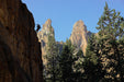 Person climbing a rocky cliff with mountains and trees in the background.