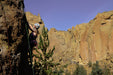 Person rock climbing on a rocky cliff with a clear blue sky.