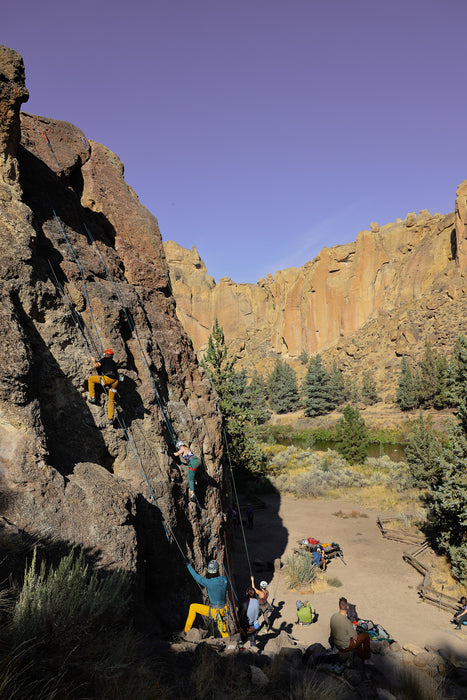 People climbing a rocky cliff with a scenic landscape in the background.
