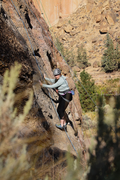 Person rock climbing on a rocky cliff face with a scenic background.