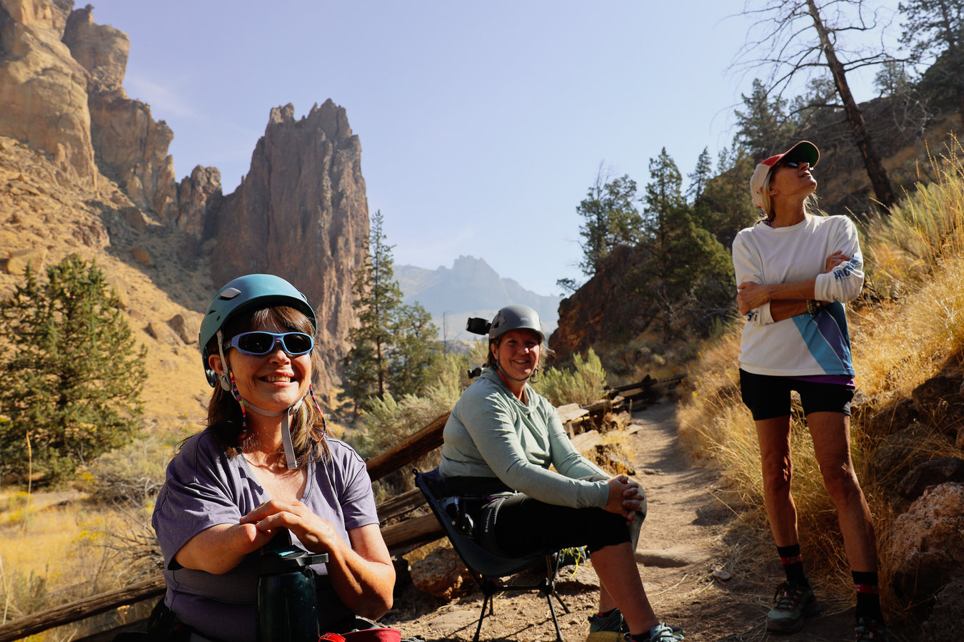 Three people on a hiking trail with mountains and trees in the background.