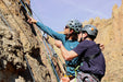 Two climbers on a rock face with helmets and ropes.