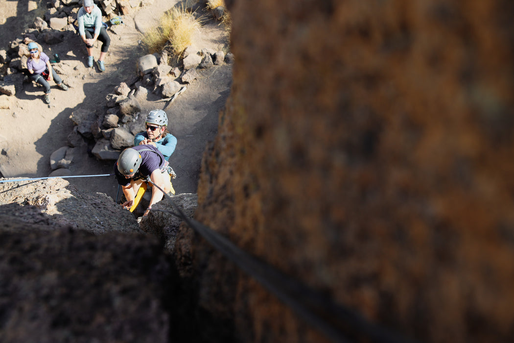 Person climbing a rocky cliff with others observing in the background