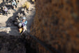 Person climbing a rocky cliff with others observing in the background