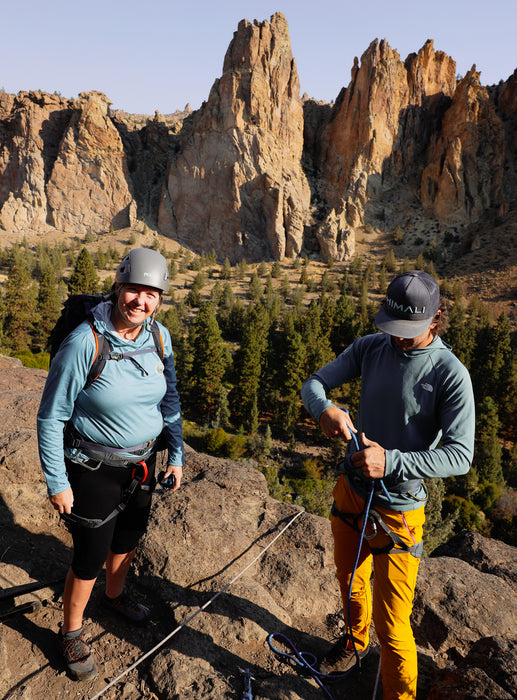 Two climbers on a rocky outcrop with mountainous landscape in the background.