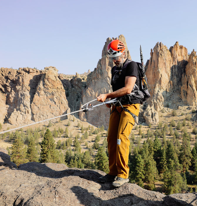 Person in climbing gear on a rocky outcrop with mountainous landscape in the background.