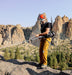 Person in climbing gear on a rocky outcrop with mountainous landscape in the background.