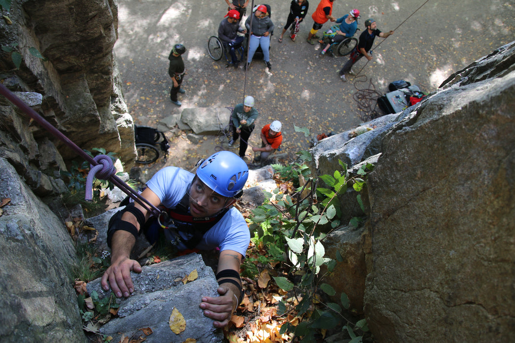 Person climbing a rocky cliff with others in the background.