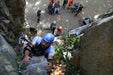 Person climbing a rocky cliff with others in the background.
