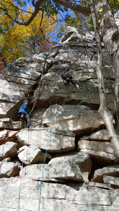 Two climbers on a rocky cliff face with autumn foliage in the background.