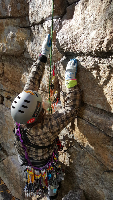 Person rock climbing on a rocky wall with climbing gear.