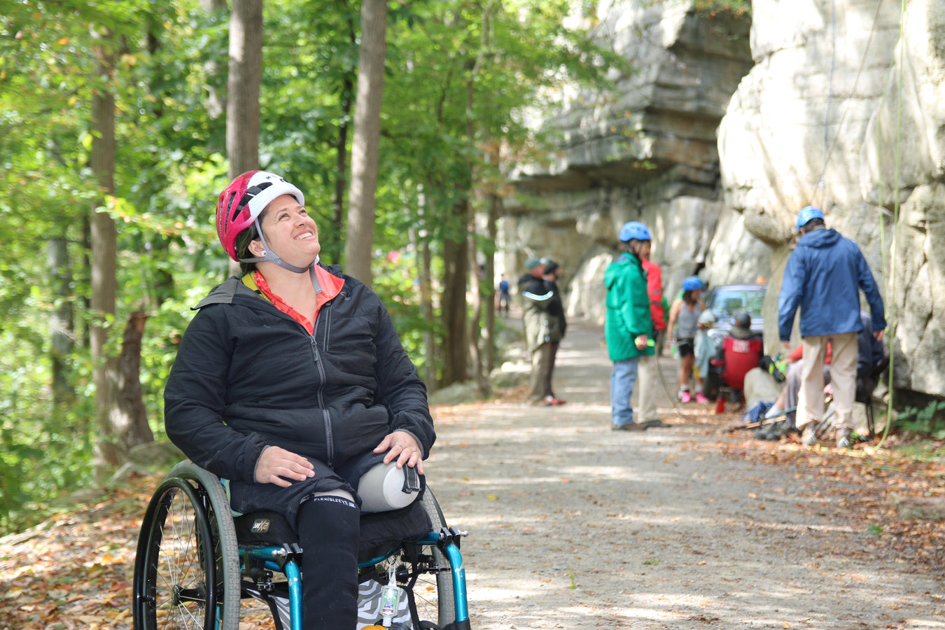 Person in a wheelchair on a trail with trees and rocks in the background.