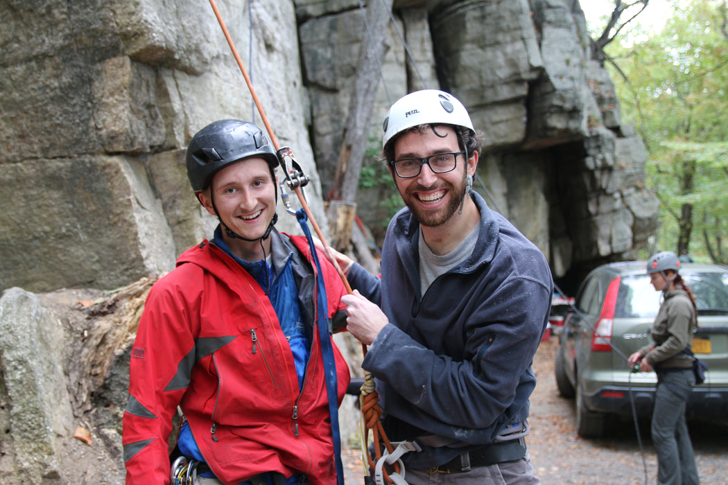 Two climbers with ropes in front of a rock formation.
