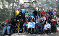 Group of people with and without disabilities posing for a photo in front of a rock wall holding the Paradox Sports Flag.
