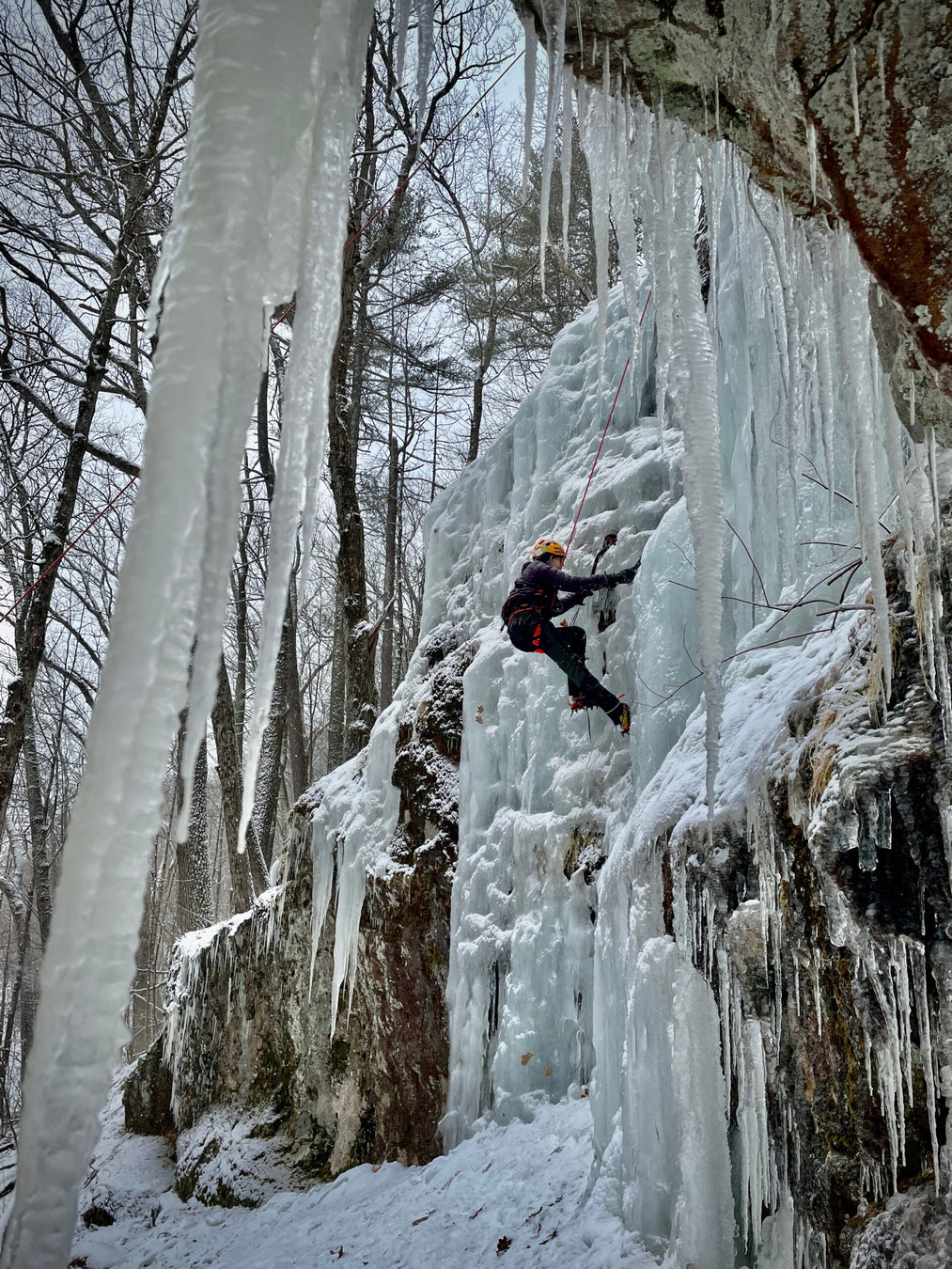 Person ice climbing a frozen waterfall in a snowy forest
