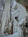 Person ice climbing a frozen waterfall in a snowy forest