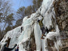 People ice climbing on a frozen waterfall with trees in the background