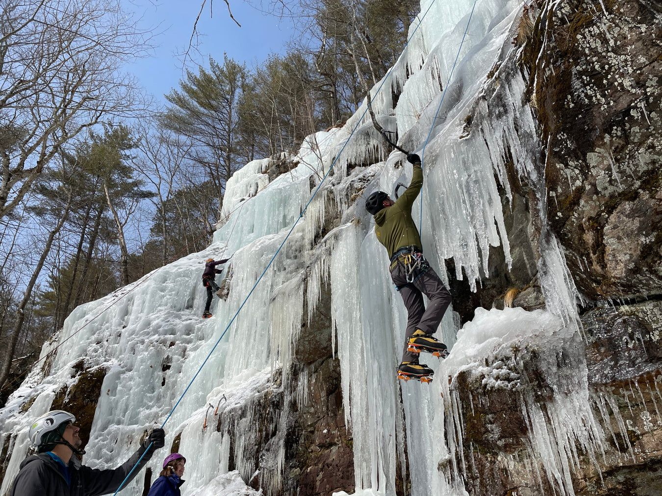 People ice climbing on a frozen waterfall with trees in the background