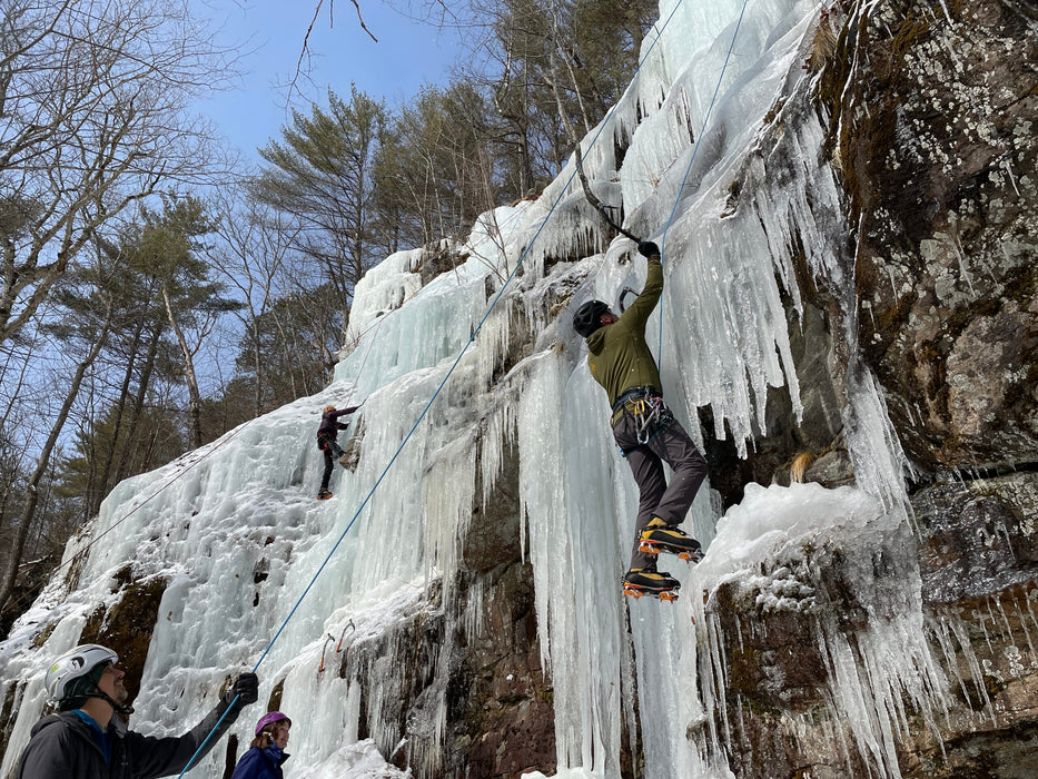 People ice climbing on a frozen waterfall with trees in the background
