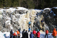 People ice climbing on a frozen waterfall in a snowy landscape.