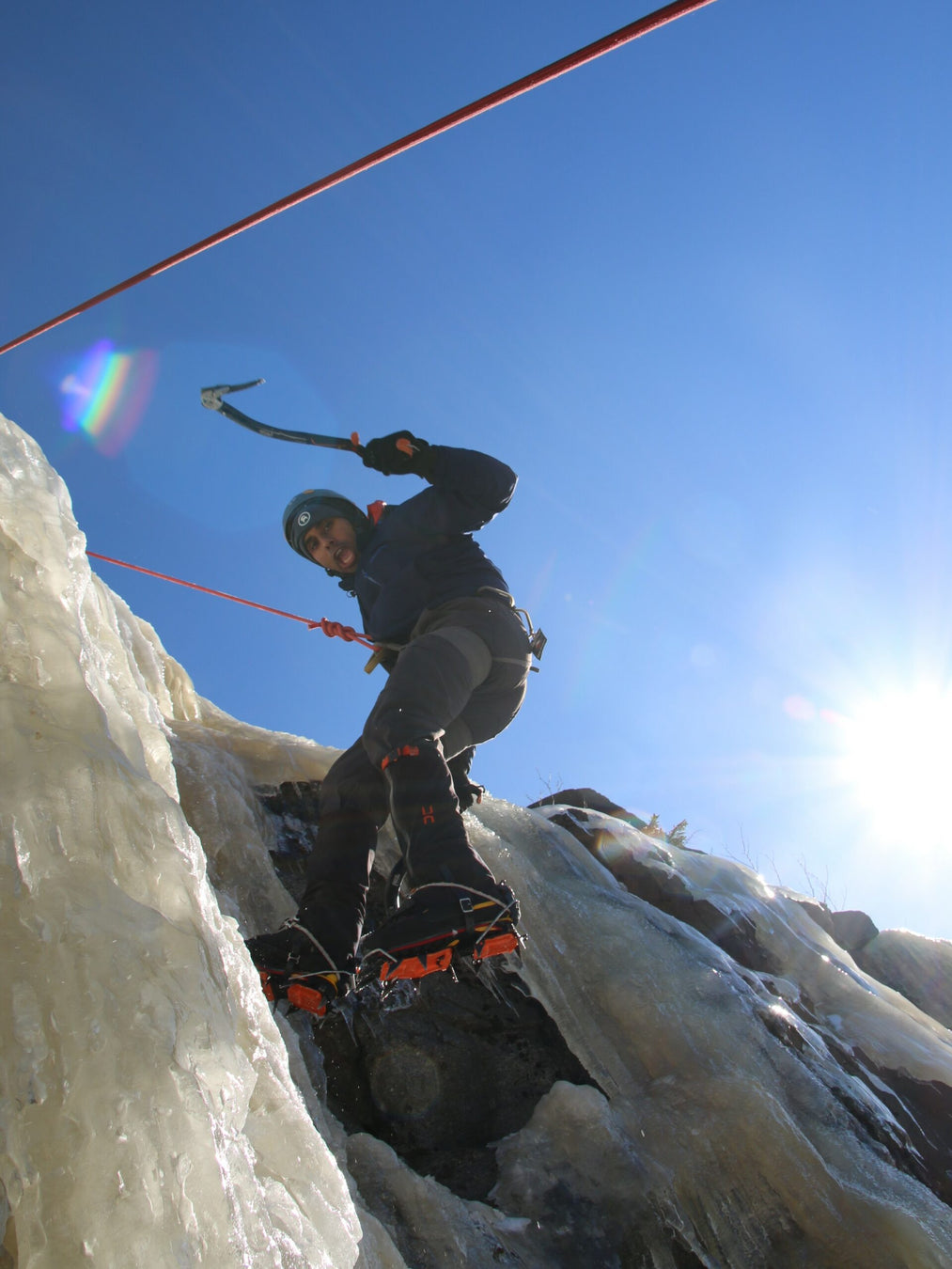Person ice climbing on a frozen waterfall with a clear blue sky.