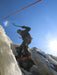 Person ice climbing on a frozen waterfall with a clear blue sky.