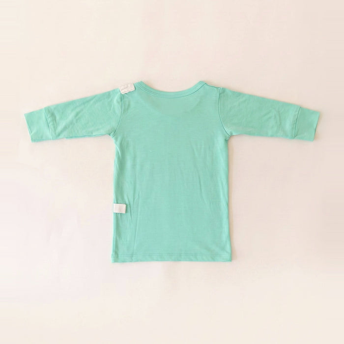 Back angle of the PediaTech Apparel LineWear Central Line Access Baby Gown in mint green (Calm Mint Edition) with white tubing guides at the shoulder and lower back, laid flat against an off-white background