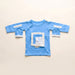 Front angle of the PediaTech Apparel LineWear Central Line Access Baby Gown in light blue (Sky Lullaby Edition) with the chest pocket flap opened to show its white lining and both sleeve openings unsnapped, laid flat against an off-white background
