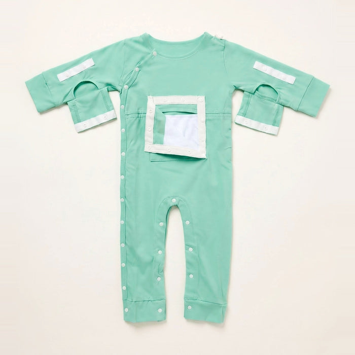 Front angle of the PediaTech Apparel LineWear Central Line Access Baby & Toddler Bodysuit in mint green (Calm Mint Edition) with the chest pocket flap opened to show its white lining and both sleeve openings unsnapped, laid flat against an off-white background