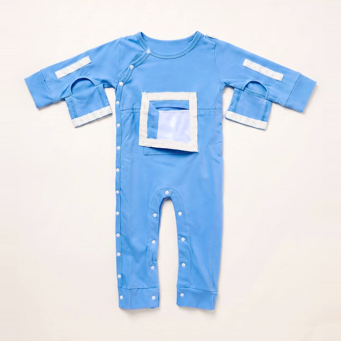 Front angle of the PediaTech Apparel LineWear Central Line Access Baby & Toddler Bodysuit in light blue (Sky Lullaby Edition) with the chest pocket flap opened to show its white lining and both sleeve openings unsnapped, laid flat against an off-white background