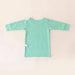 Back angle of the PediaTech Apparel TubeWear G/J Tube Access Baby Gown in mint green (Calm Mint Edition) with white tubing guides at the shoulder and lower back, laid flat against an off-white background