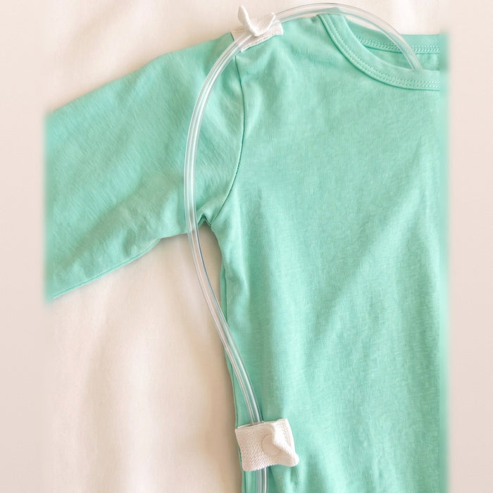 Close-up of clear tubing threaded through the white guides at the shoulder and lower back of the PediaTech Apparel TubeWear G/J Tube Access Baby Gown in mint green (Calm Mint Edition)
