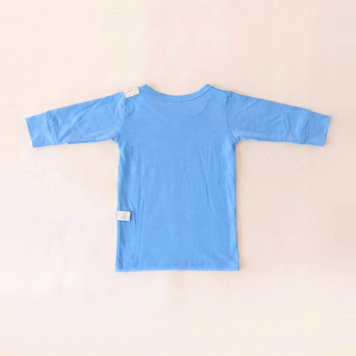 Back angle of the PediaTech Apparel TubeWear G/J Tube Access Baby Gown in light blue (Sky Lullaby Edition) with white tubing guides at the shoulder and lower back, laid flat against an off-white background