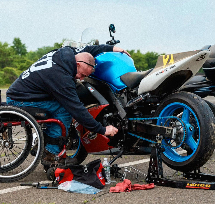 Person in a wheelchair working on a blue motorcycle with a clear sky background