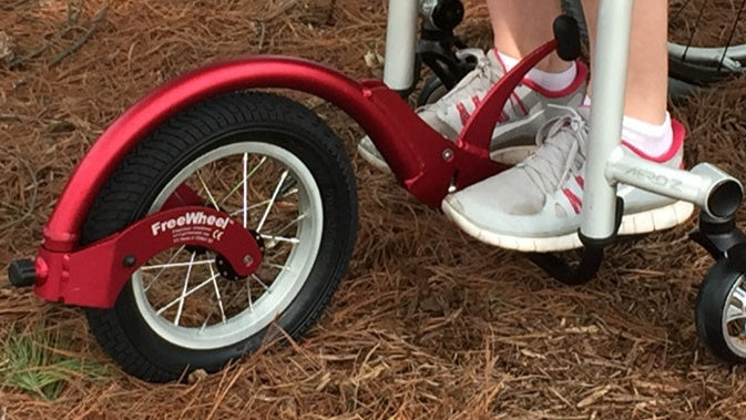 Detail of a FreeWheel Wheelchair Attachment Red on a wheelchair outdoors.