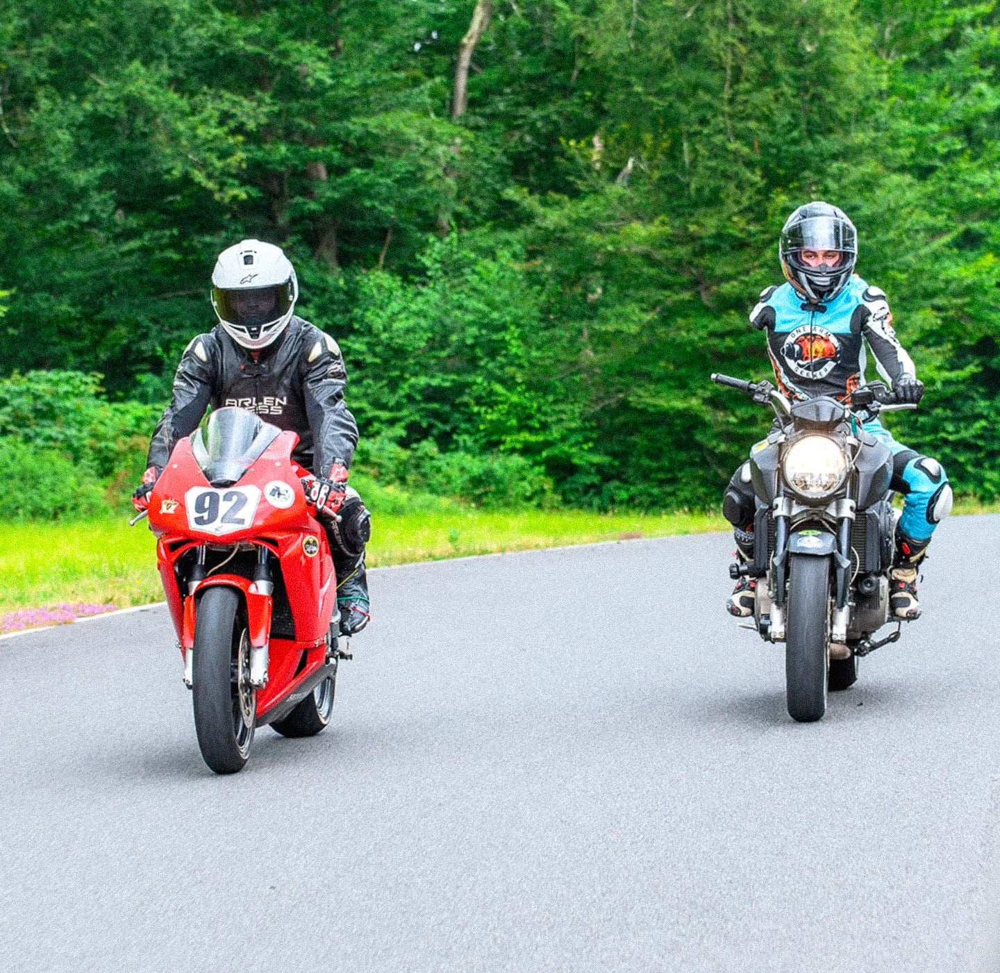 Two adaptive motorcyclists on a road with greenery in the background