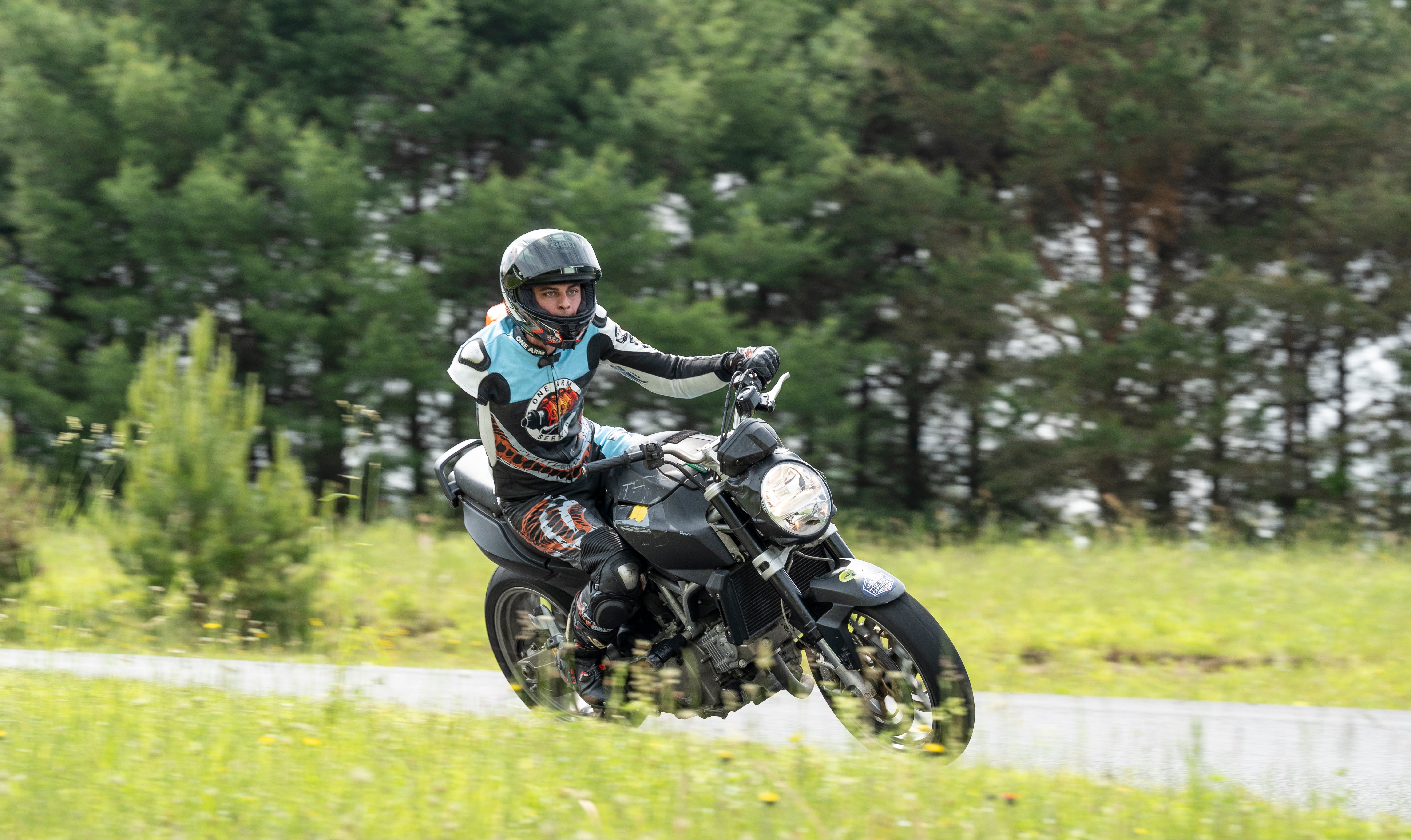 Person riding a motorcycle with an amputated right arm on a track with trees in the background