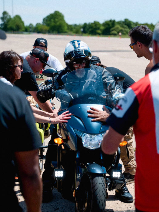 Person on a motorcycle being assisted by others in an outdoor setting