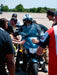 Person on a motorcycle being assisted by others in an outdoor setting