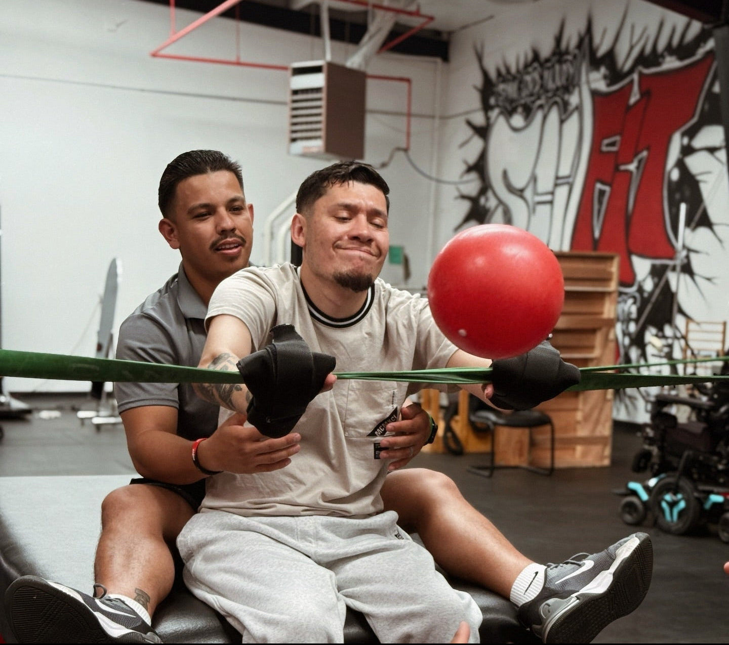 A person with spinal cord injury at SCI-FIT throwing a ball by releasing it from an elastic band with support from SCI-FIT trainers.