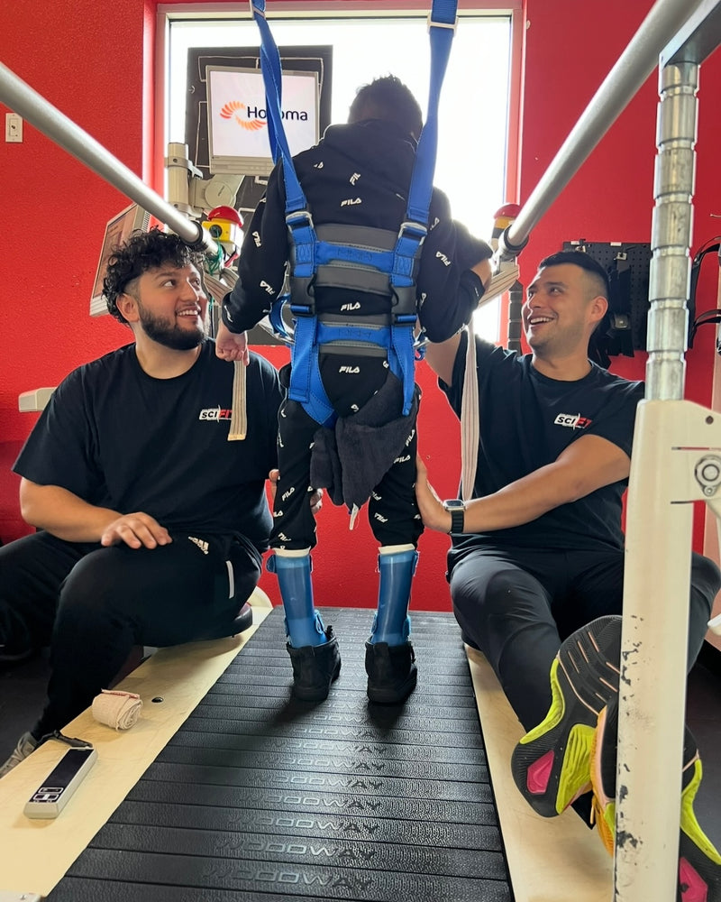 Person walking with a harness with assistance from two individuals from SCI-FIT