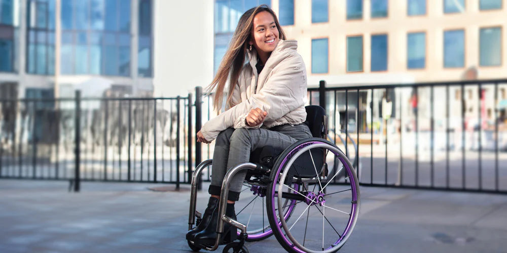 Person in a wheelchair with Spinergy XLX  Wheels smiling outdoors with modern buildings in the background