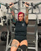SuZanne Jacobsen performing a machine shoulder press while wearing the Severed Society® Members Only T-Shirt.